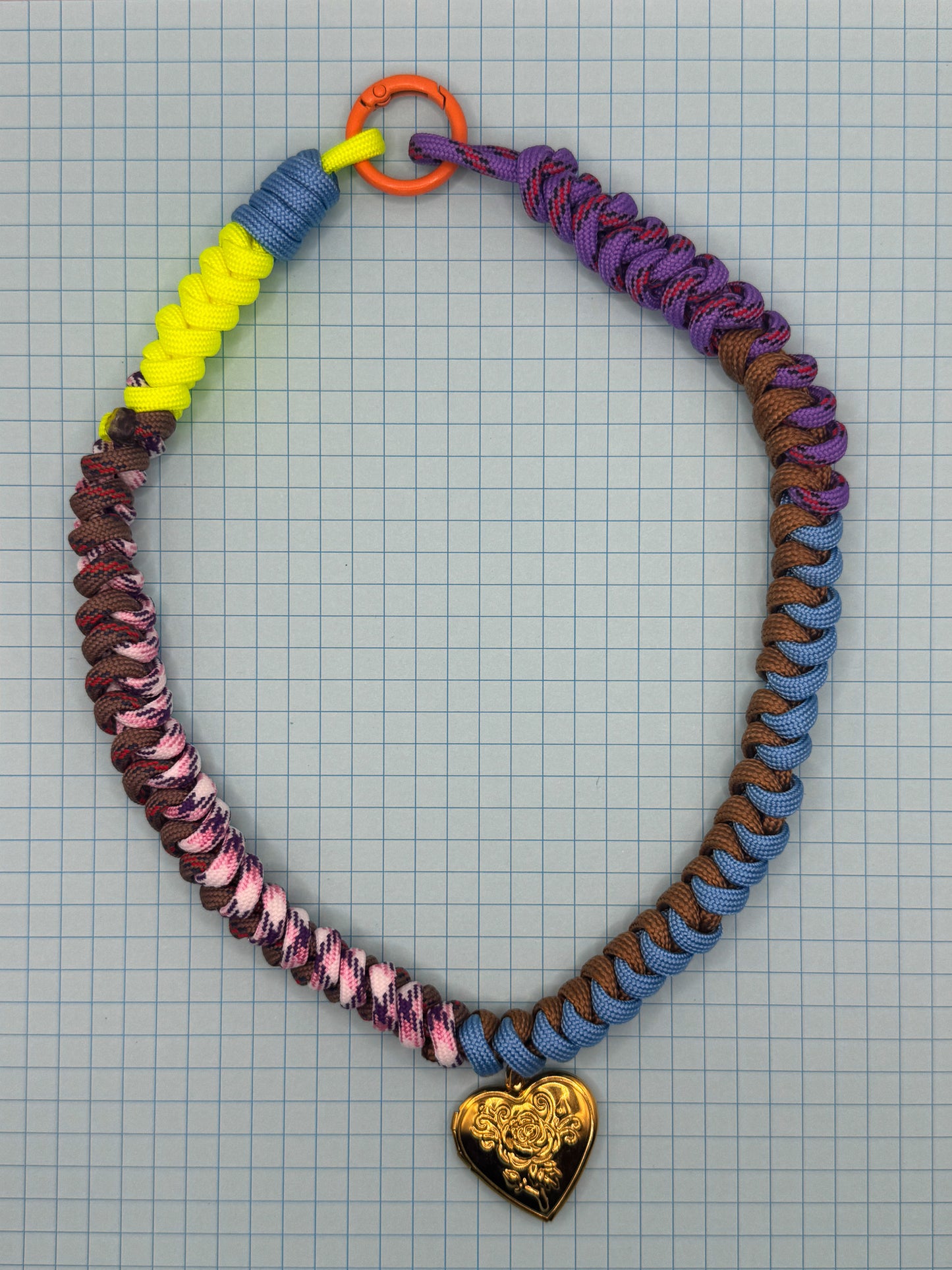 Colorful paracord necklace with a heart-shaped pendant on a grid background