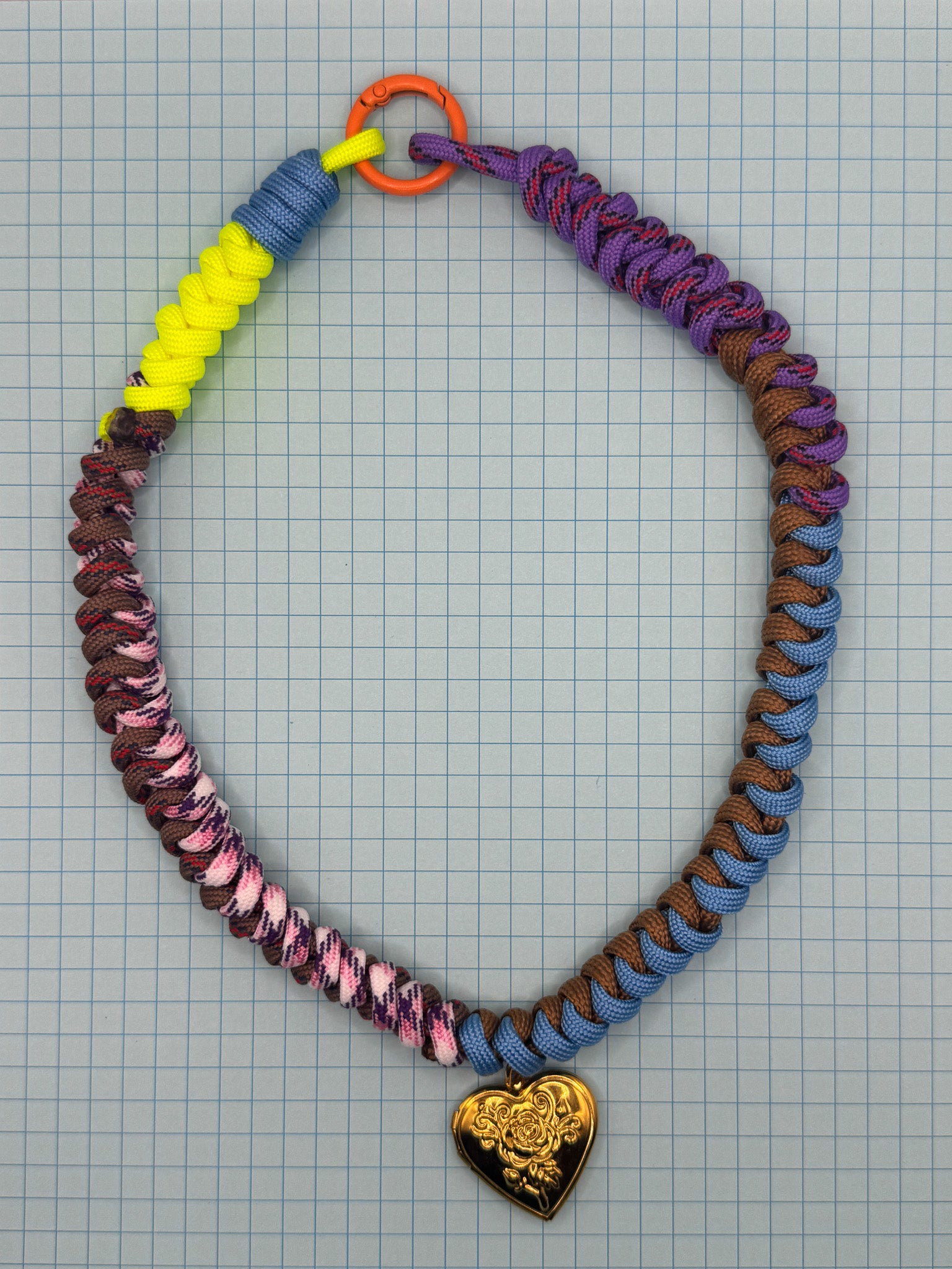 Colorful paracord necklace with a heart-shaped pendant on a grid background