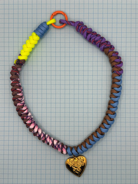 Colorful paracord necklace with a heart-shaped pendant on a grid background