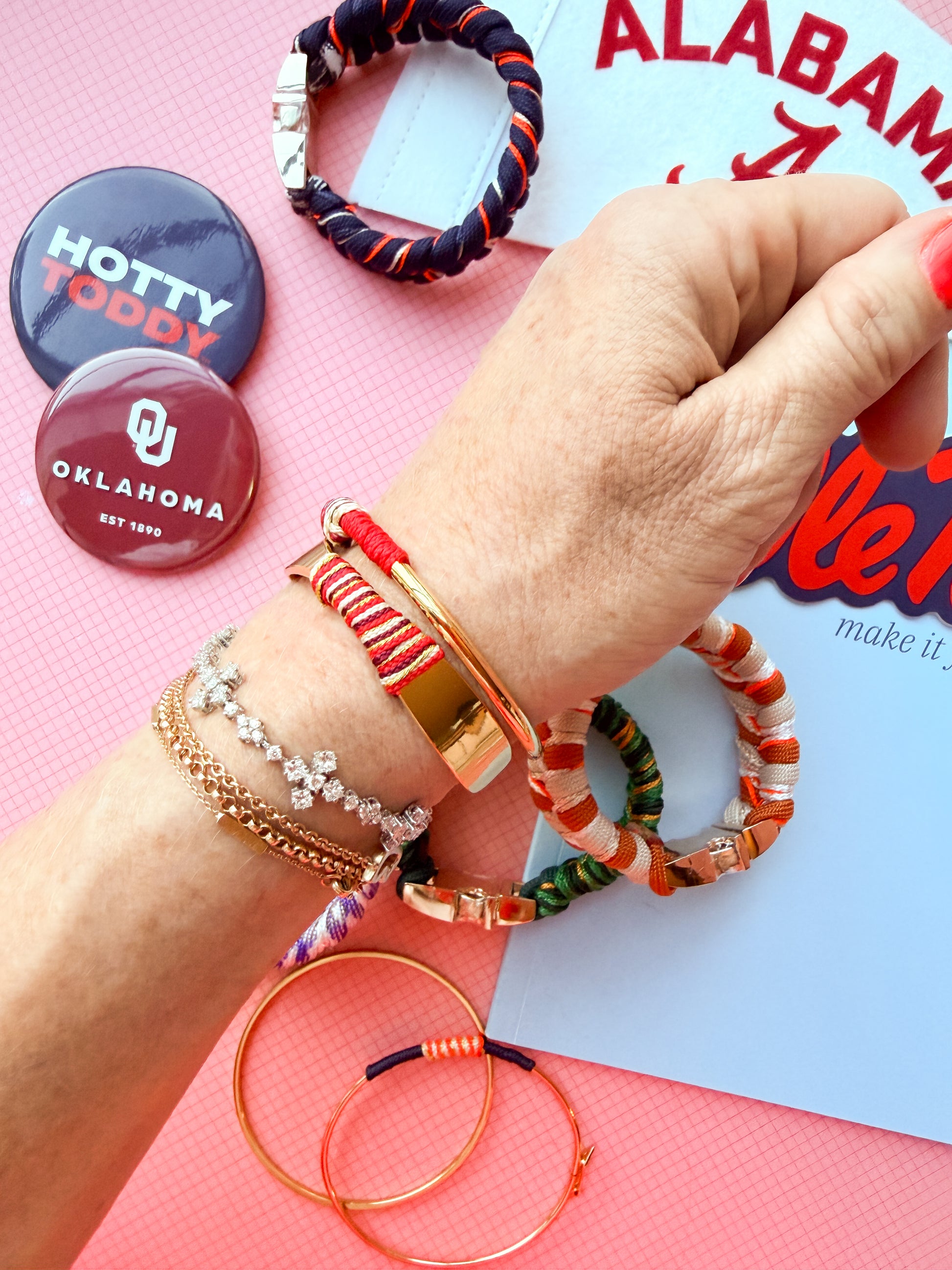 Hand wearing multiple bracelets with colorful designs on a pink surface